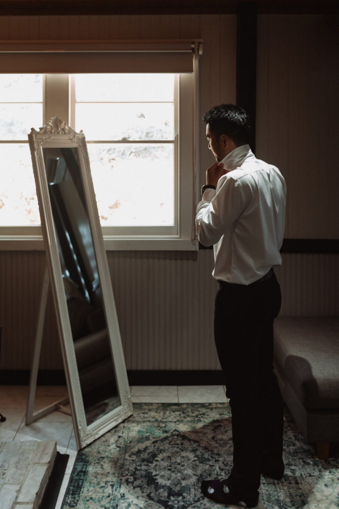 Groom gets ready in the mirror for his wedding